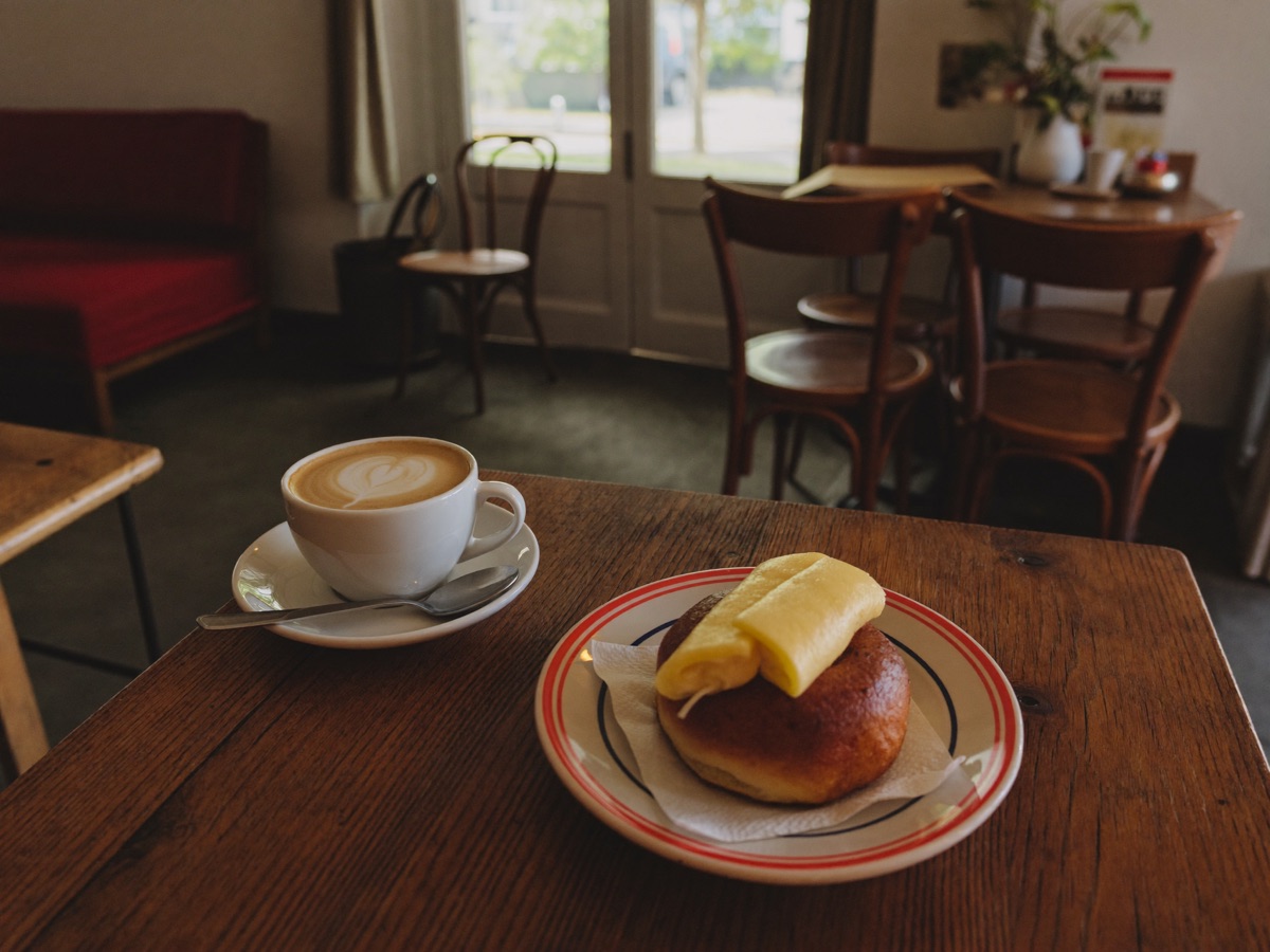 A flat white and morning roll on a cafe table